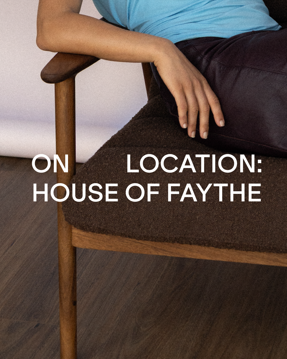 A person reclining on a mid-century modern wooden armchair with a dark brown bouclé seat cushion, with large white text reading 'ON LOCATION: HOUSE OF FAYTHE' overlaid across the center.